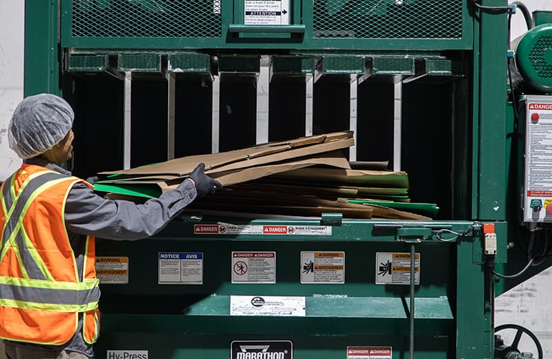 MTE Logistix employee places cardboard boxes into bailer to be compressed for recycling